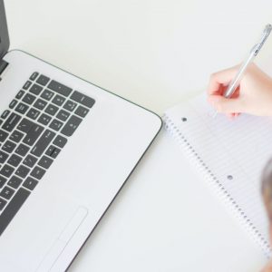 A student begins to make notes on paper by a laptop.
