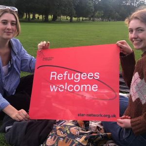 Two students hold a banner that says 'Refugees welcome'